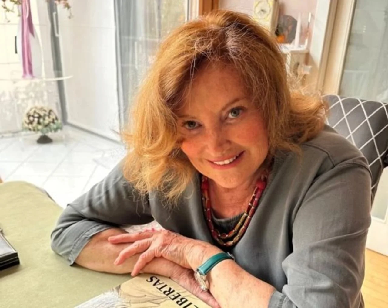 Nasmijana Tereza Kesovija sjedi za stolom s knjigom Libertas.