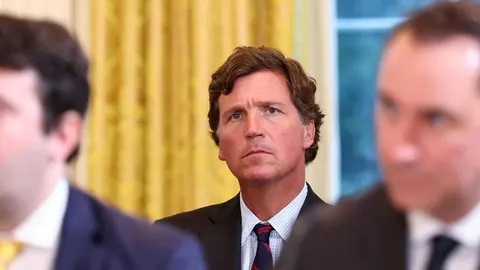 Tucker Carlson ozbiljnog izraza lica u odijelu s prugastom kravatom.