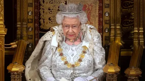 Kraljica Elizabeta II. s krunom i u svečanoj odori sjedi na prijestolju