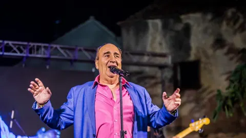 Mladen Grdović pjeva na pozornici u plavom sakou i ružičastoj košulji.