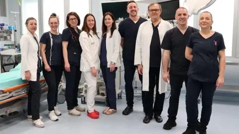 Grupa medicinskih djelatnika u bolničkom okruženju pored medicinske opreme.