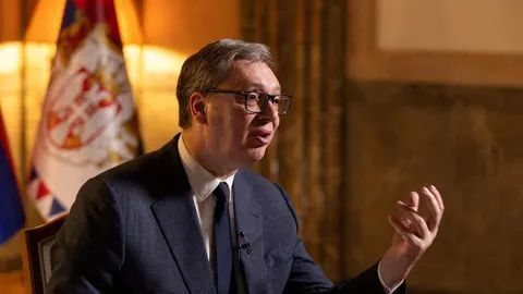 Aleksandar Vučić u tamnom odijelu s naočalama govori i gestikulira rukom.