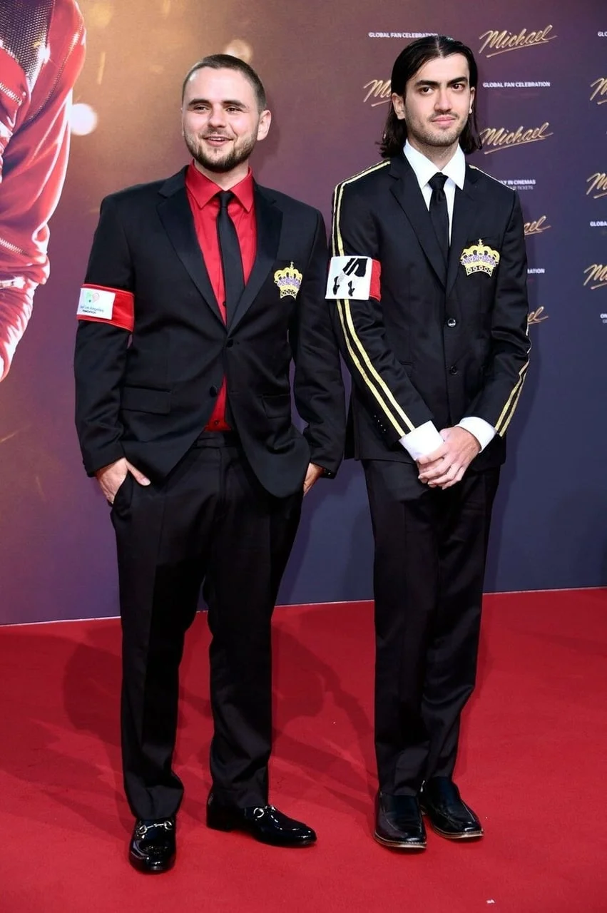 Sinovi Michaela Jacksona u tamnim odijelima s crvenim trakama na rukavu.