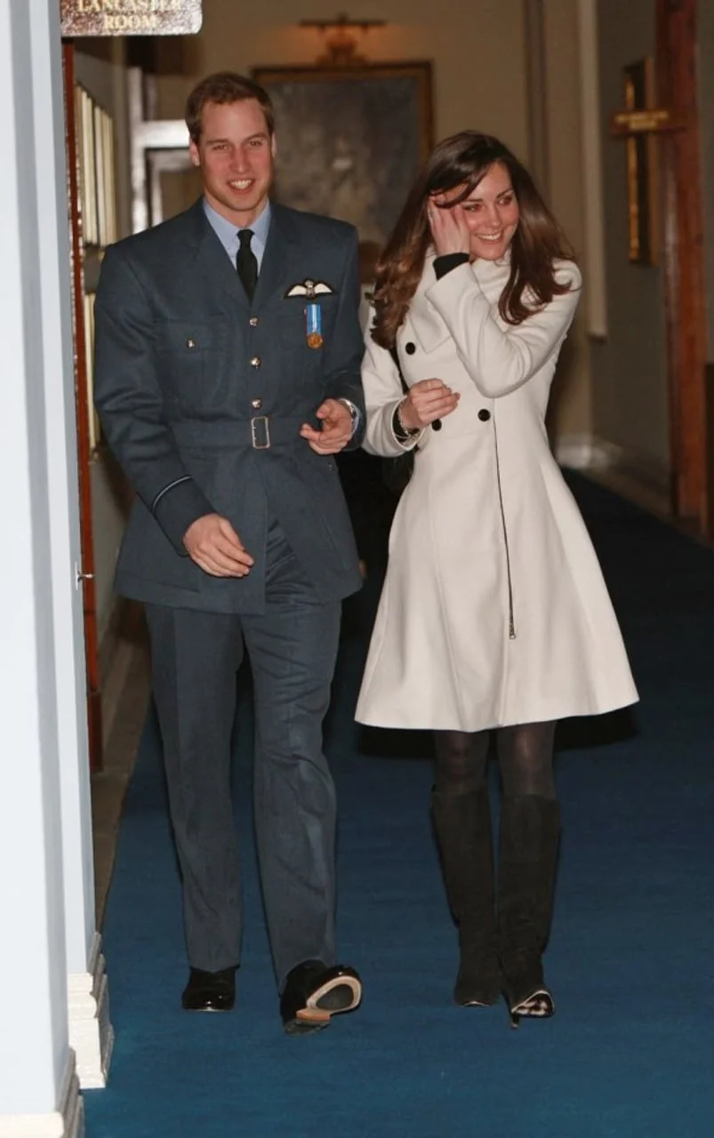 Mladi princ William u uniformi i Kate Middleton u bijelom kaputu u hodniku.