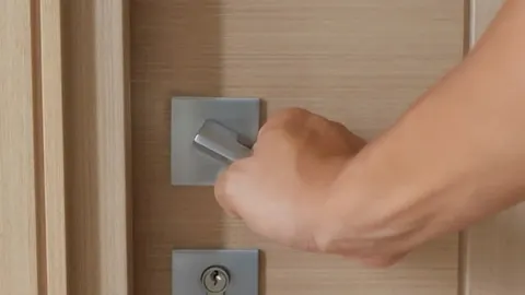 Ruka dodiruje metalnu kvaku na drvenim sobnim vratima.