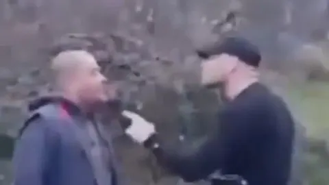 Muškarac u crnoj odjeći s kapom unosi se u lice drugom muškarcu na ulici.