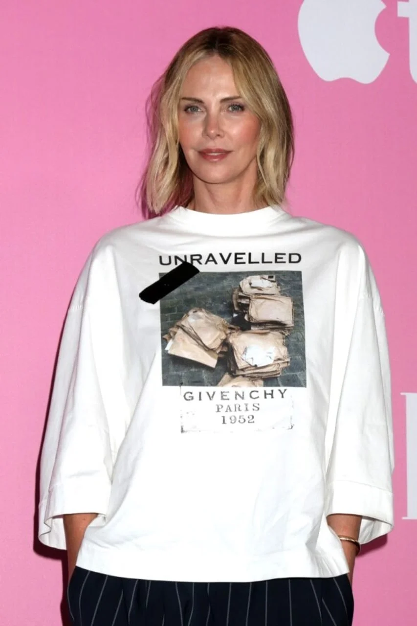 Charlize Theron pozira ispred ružičaste pozadine u bijeloj Givenchy majici.