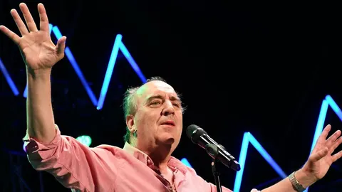 Mladen Grdović pjeva na pozornici s podignutom rukom ispred plavih svjetala.