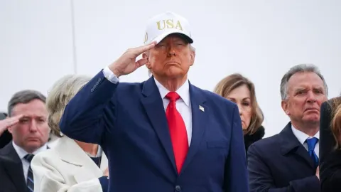 Donald Trump u tamnom odijelu s bijelom kapom salutira tijekom javnog događaja.