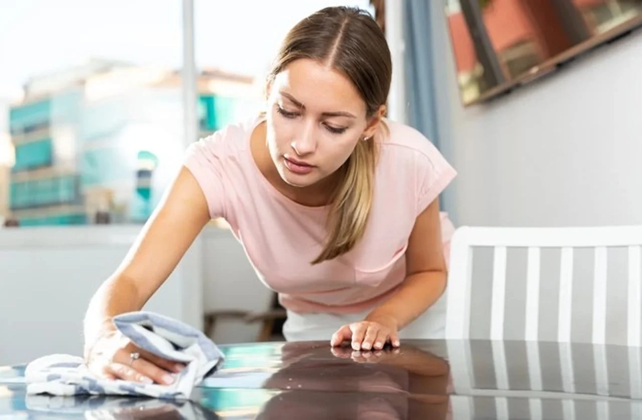 Djevojka u ružičastoj majici briše tamnu radnu površinu pamučnom krpom.
