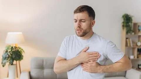 Muškarac se drži za prsa s bolnim izrazom lica u dnevnom boravku.