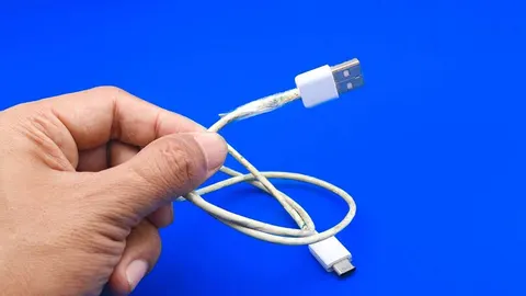 Ruka drži oštećeni bijeli USB kabel s vidljivim žicama na plavoj pozadini.
