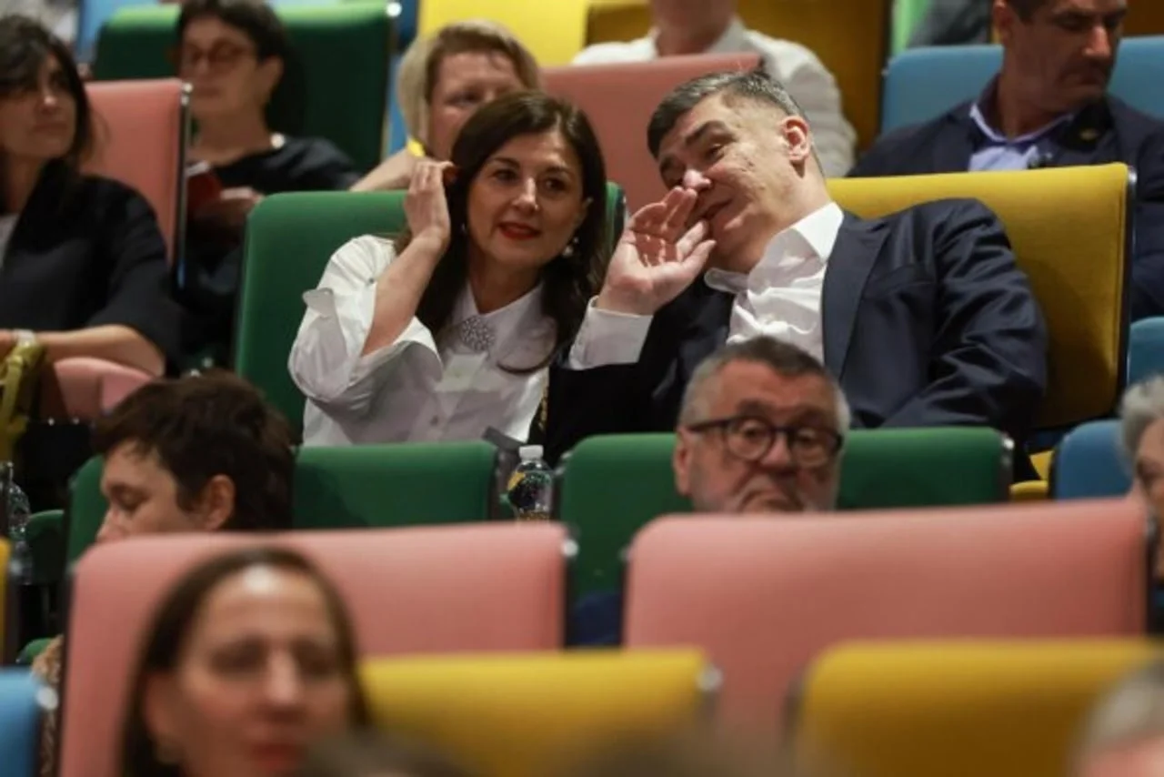 Predsjednički par sjedi u dvorani i šapuće tijekom događaja.