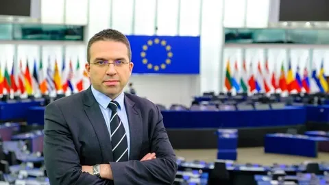 Tomislav Sokol u odijelu ispred zastava Europske unije.