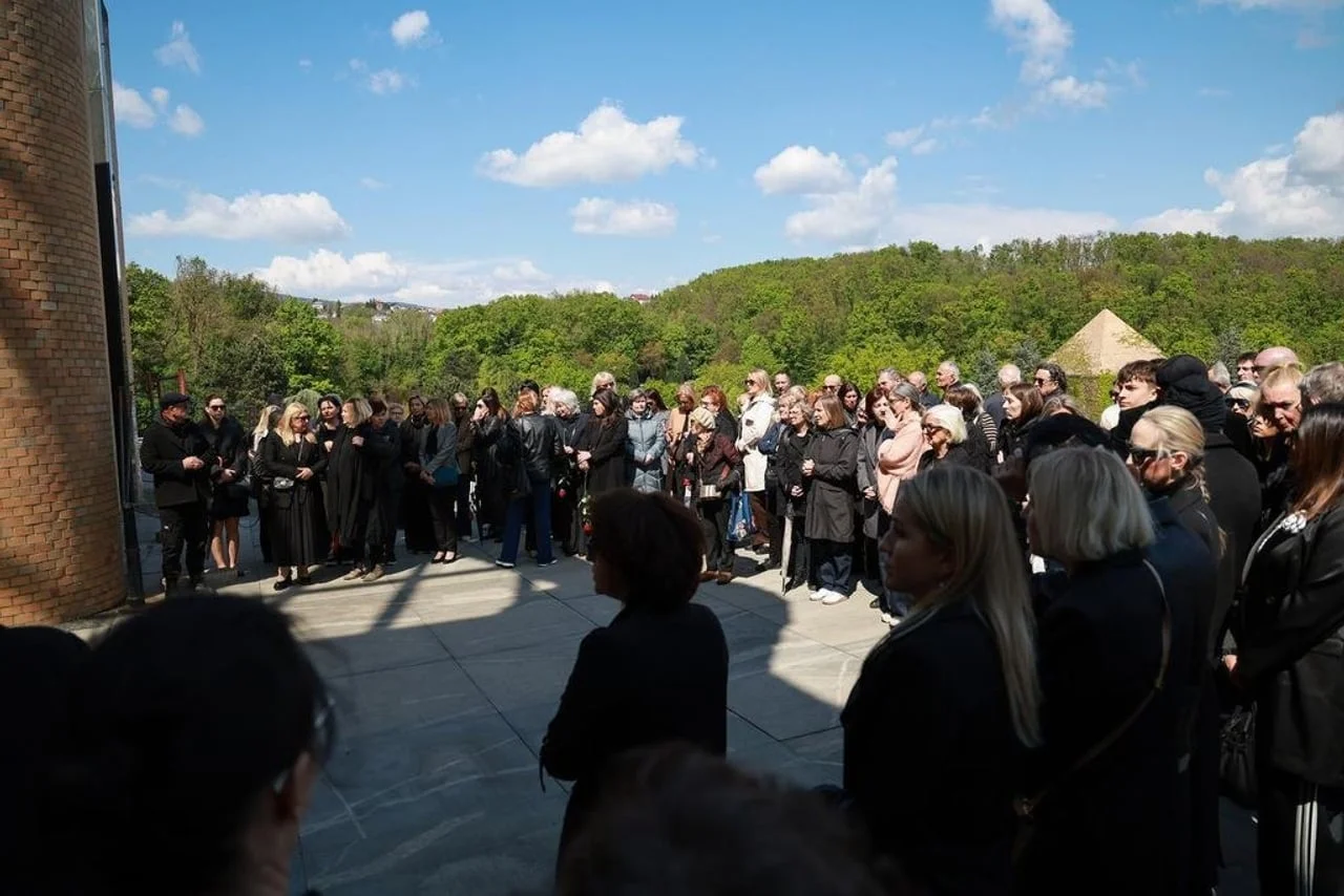 Veliki broj ljudi okupljen ispred zgrade zagrebaćkog krematorija po sunćanom vremenu.