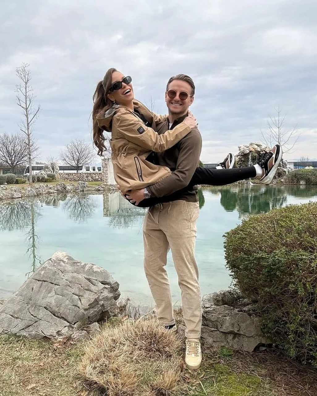 Ivan Rakitić nosi nasmijanu Raquel Mauri u prirodi pored vode.