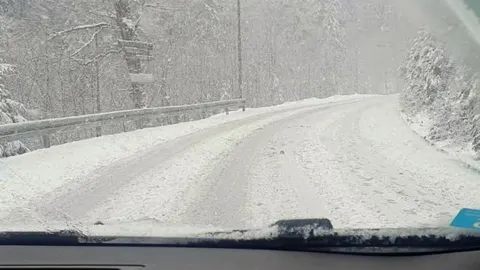 Planinska cesta prekrivena snijegom snimljena iz unutrašnjosti automobila.