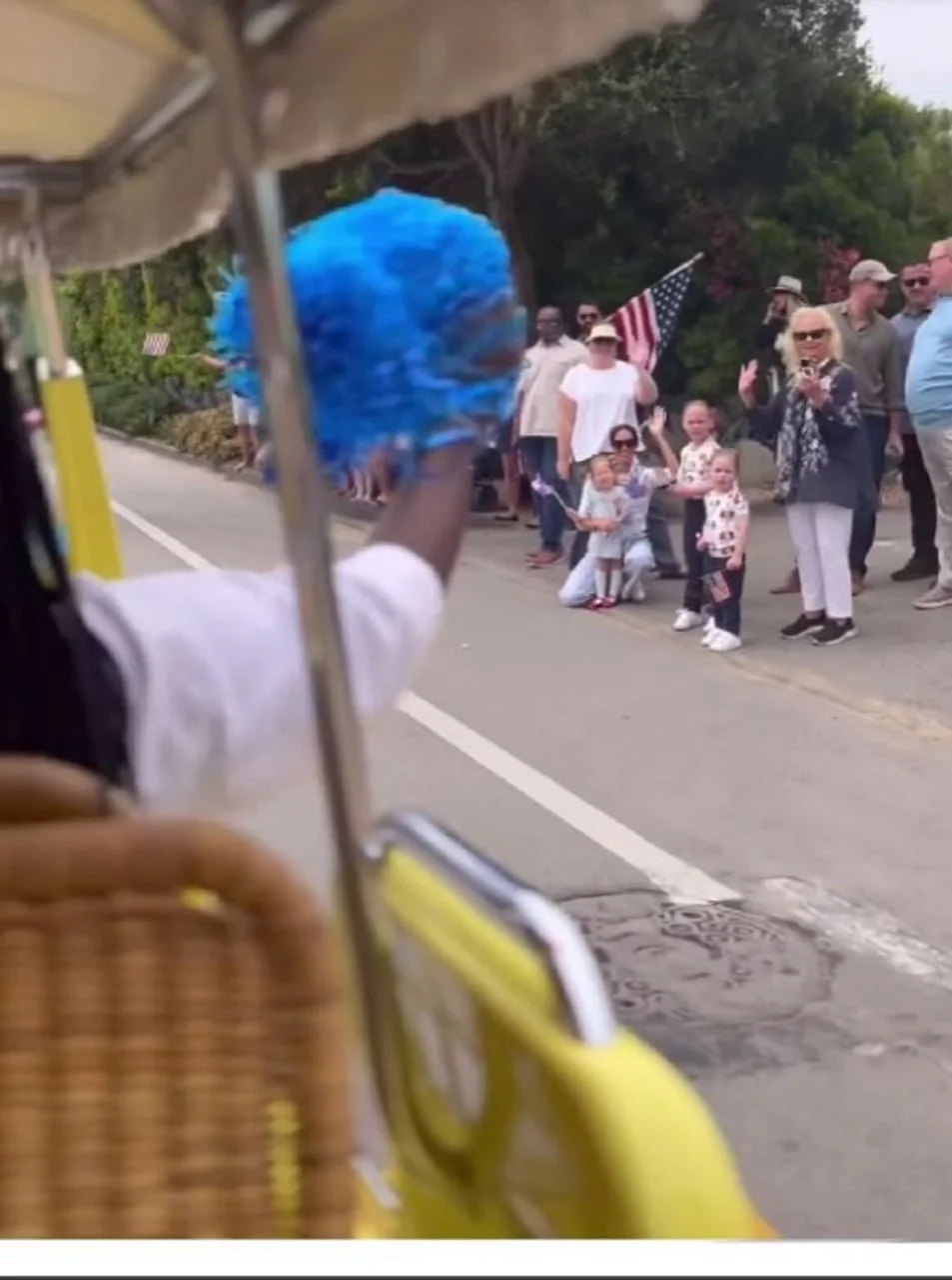 Mutni prikaz ljudi koji mašu uz cestu tijekom parade.