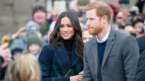 Meghan Markle i princ Harry u hodu okruženi mnoštvom ljudi.