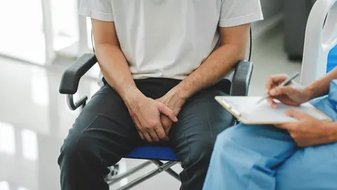 Muškarac sjedi na pregledu kod liječnika držeći ruke u krilu.