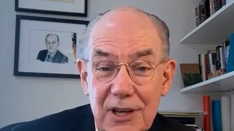 John Mearsheimer s naočalama govori ispred police s knjigama.