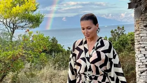 Nina Badrić u haljini s uzorkom stoji ispred mora i duge.