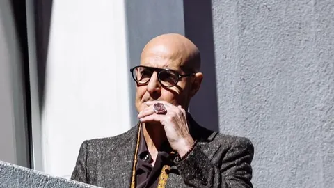 Glumac Stanley Tucci s naočalama i u sivom sakou gleda u daljinu.