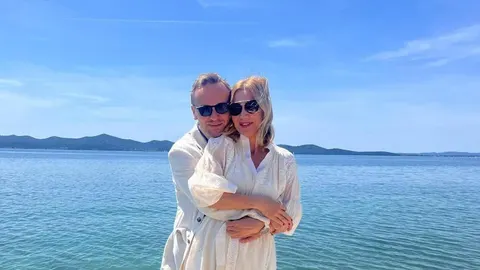 Ecija Ojdanić i suprug Robert Orhel zagrljeni na obali mora pod sunčanim nebom.