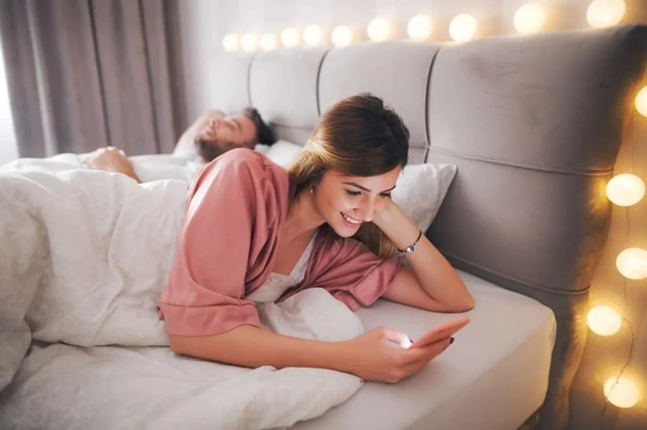 Žena koristi pametni telefon u krevetu dok muškarac spava