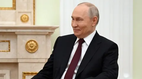 Vladimir Putin u odijelu sjedi ispred kamina u Kremlju.