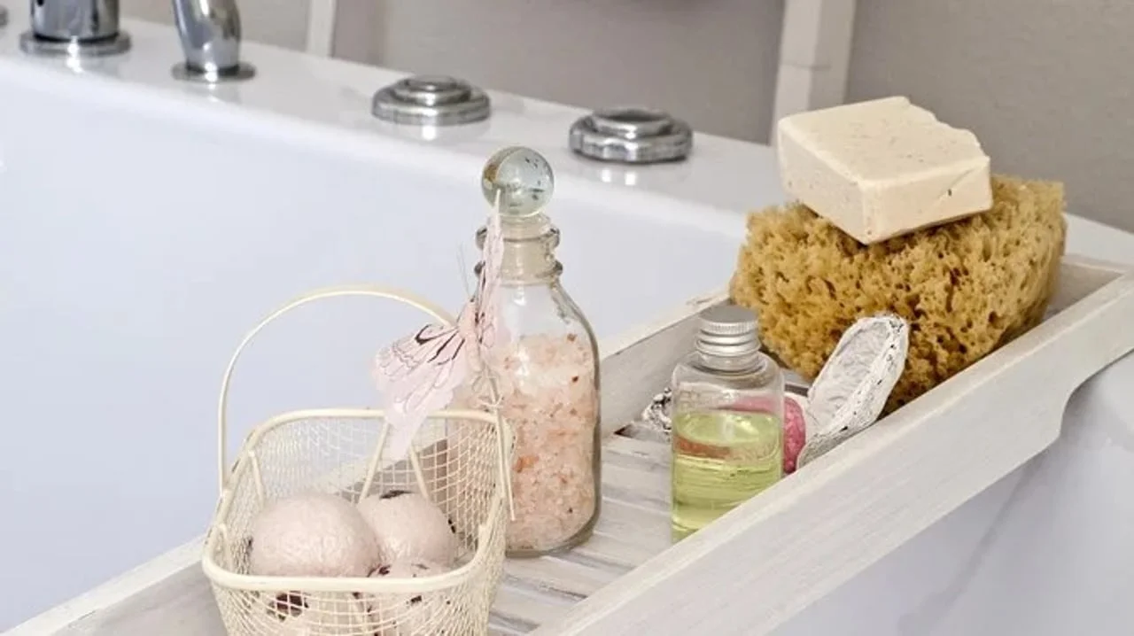 Drveni držač iznad kade s kozmetičkim proizvodima, soli i spužvom.