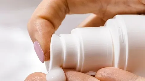 Ruka pritišće dozator bijele bočice s gustom bijelom kremom.