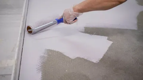 Ruka s valjkom nanosi sivu boju na betonski pod garaže