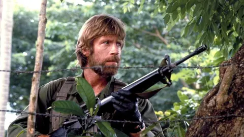 Chuck Norris s puškom u vojnoj odori iza bodljikave žice