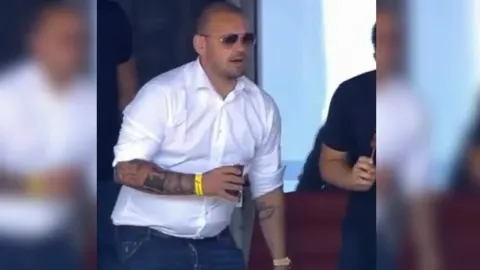 Wesley Sneijder u bijeloj košulji s naočalama i tetovažama na tribini.