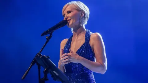 Danijela Martinović u plavoj haljini sa šljokicama pjeva na pozornici s mikrofonom.