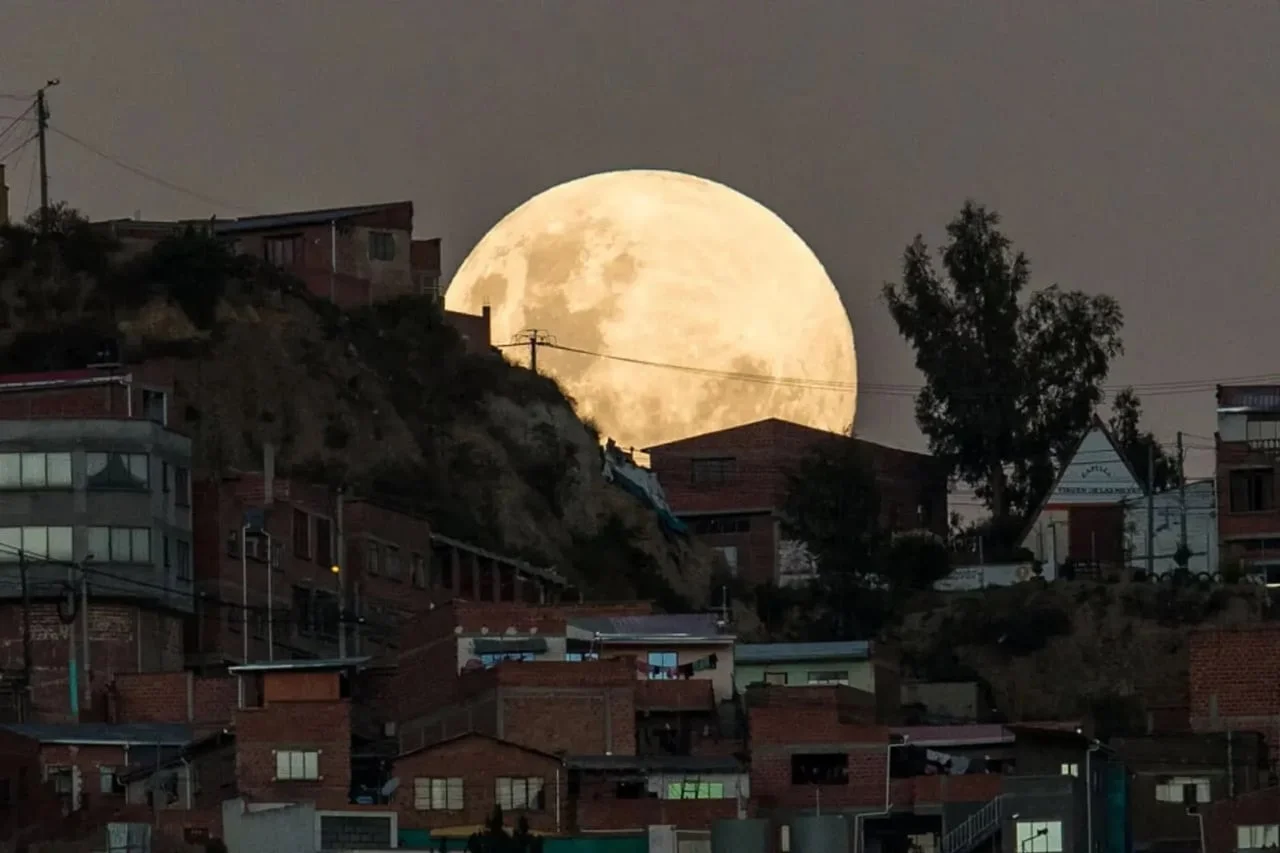 Veliki puni Mjesec izlazi iza stambenih zgrada na brdu u sumrak