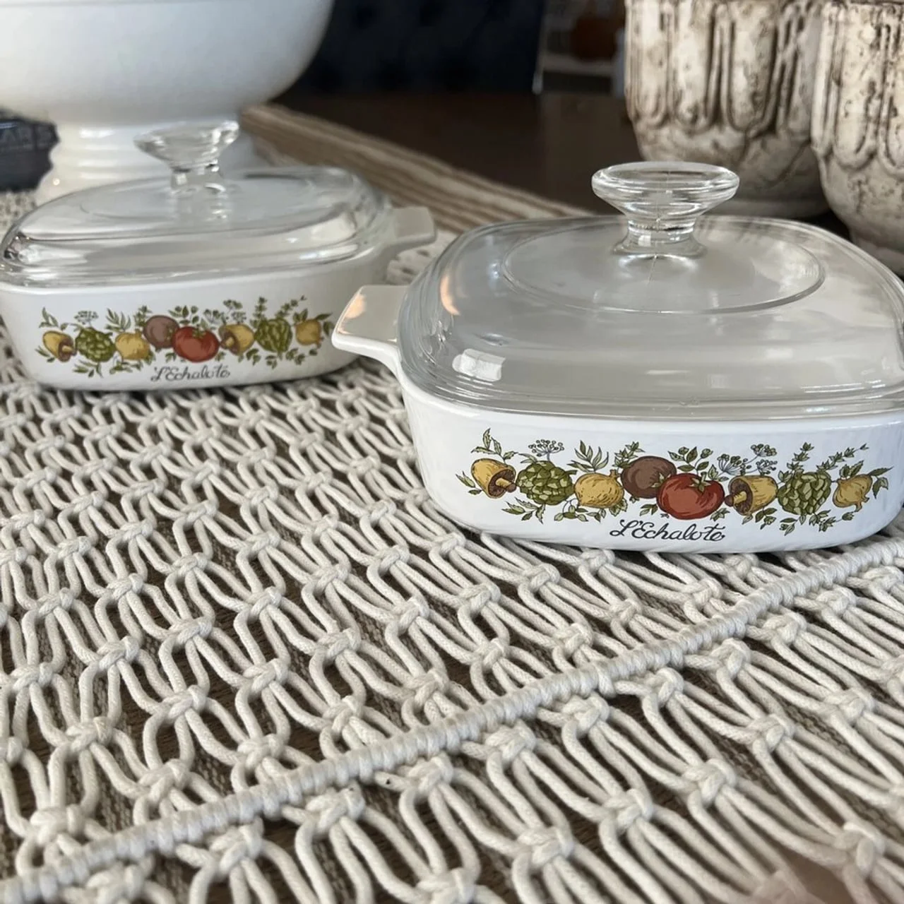 Dvije bijele keramičke posude za pečenje s cvjetnim uzorkom i staklenim poklopcima.