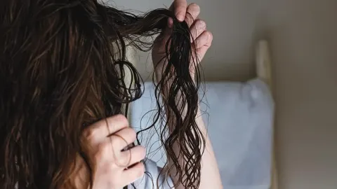 Ruke prolaze kroz mokru i zamršenu smeđu kosu ispred bijelog jastuka.