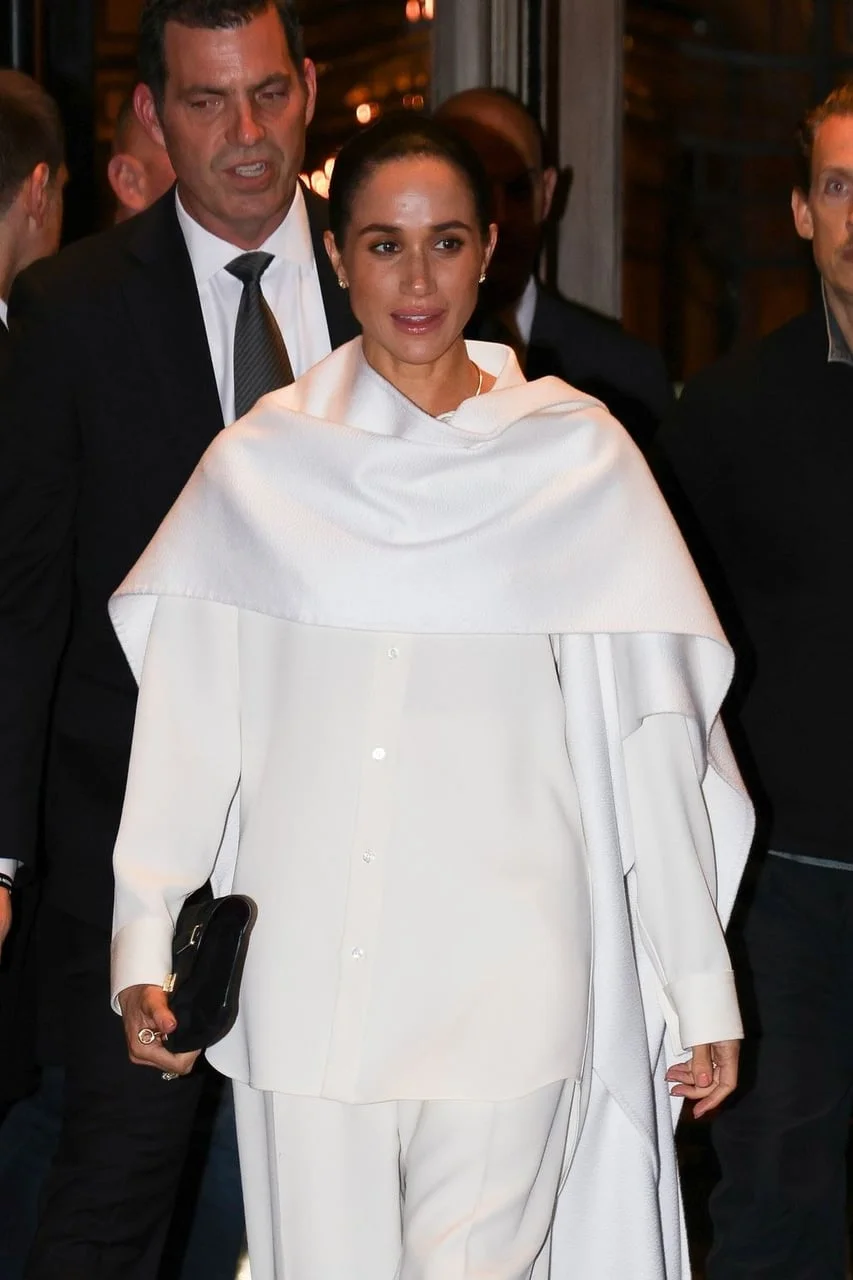 Meghan Markle u bijelom kompletu s ogrtačem izlazi iz zgrade.