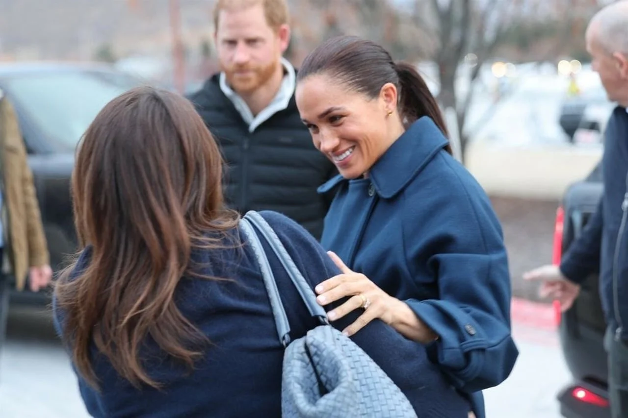 Meghan Markle se smiješi dok grli ženu na otvorenom.