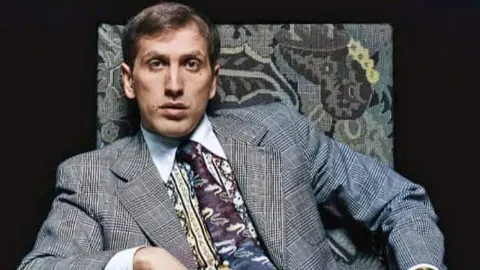 Bobby Fischer u sivom odijelu i šarenoj kravati sjedi u naslonjaču.