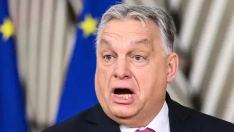 Viktor Orbán tijekom govora s otvorenim ustima ispred zastava Europske unije.