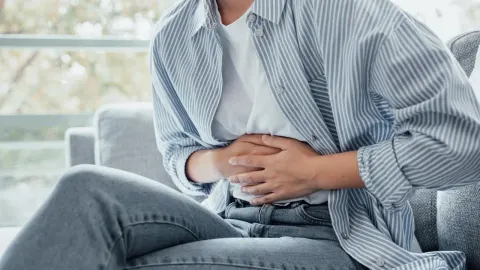 Osoba sjedi na kauču i drži se za trbuh zbog bolova i nadutosti