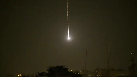 Svijetleći trag rakete na tamnom noćnom nebu iznad grada.