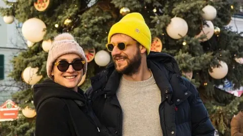 Marko Mrkić i supruga Antea nasmiješeni ispred okićenog božićnog drvca.