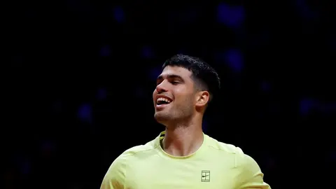 Carlos Alcaraz u žutoj sportskoj majici gleda u stranu s blagim smiješkom.