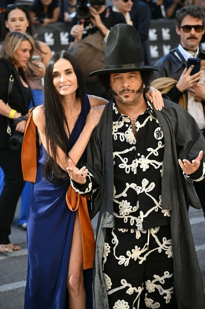 Demi Moore pozira s muškarcem u ekscentričnom odijelu s velikim šeširom.