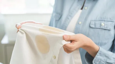 Ruke drže bijelu košulju s vidljivom masnom mrljom na tkanini.