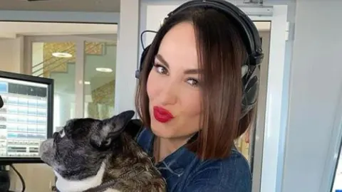 Tatjana Jurić sa slušalicama u radijskom studiju drži psa u naručju.